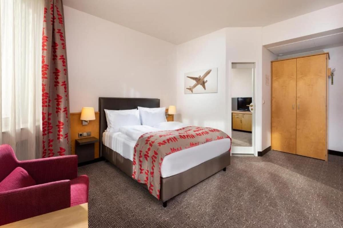 A hotel room with a bed, a desk, a chair, a wardrobe, and a television.