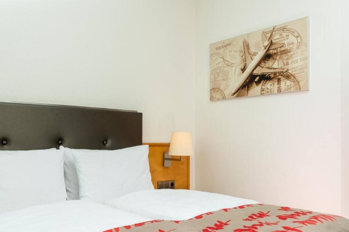 A hotel room with a bed, a nightstand with a lamp, and a wall-mounted artwork.