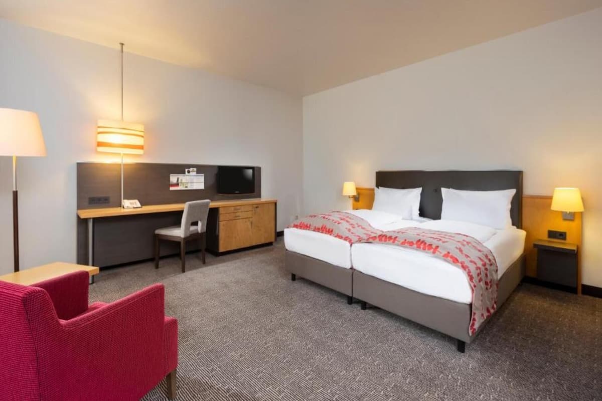 A hotel room with a bed, desk, chair, and two bedside lamps.
