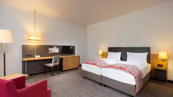 A hotel room with a bed, desk, chair, and two bedside lamps.