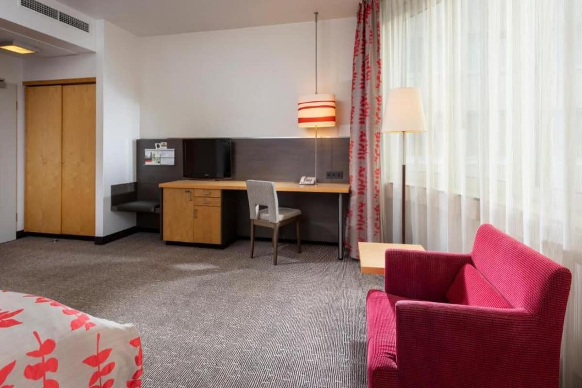 A hotel room with a desk, chair, TV, and a red sofa.