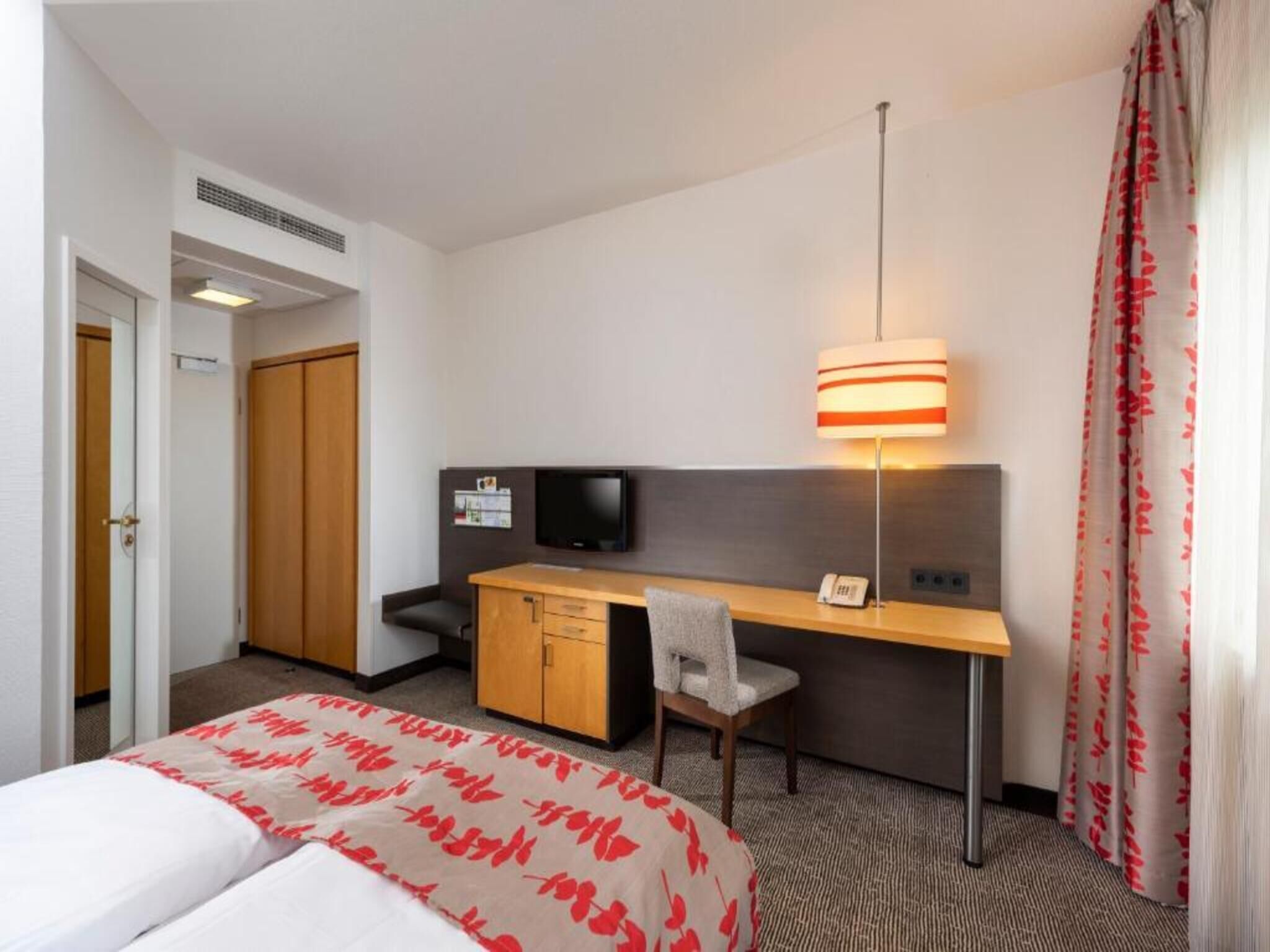 Een hotelkamer met een bed, bureau, stoel, televisie en een lamp.