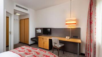 Een hotelkamer met een bed, bureau, stoel, televisie en een lamp.