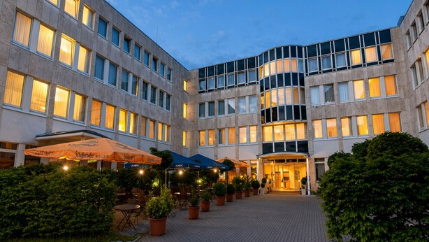 Un patio de hotel con plantas en macetas, asientos al aire libre y la entrada del edificio.