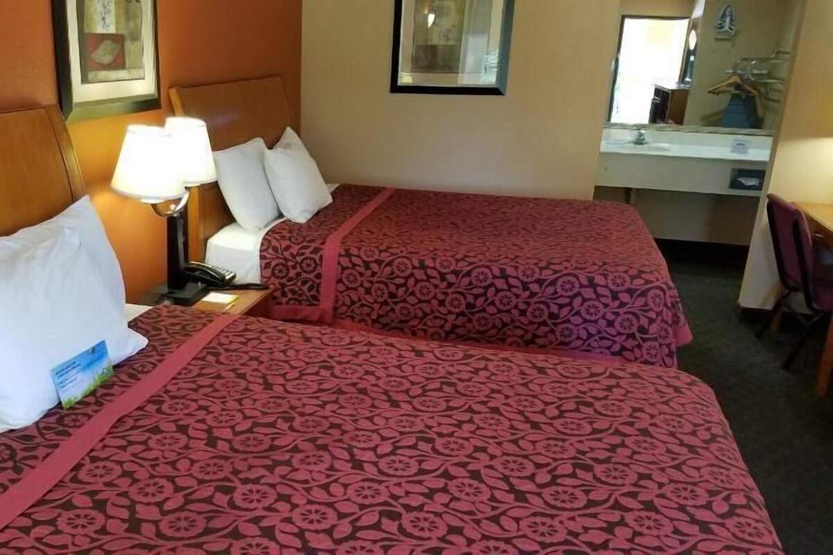 A hotel room with two beds, a desk, a chair, a lamp, and a mirror.