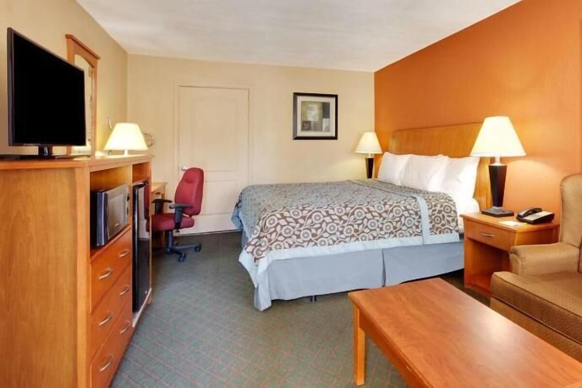 A hotel room with a bed, a desk, a chair, a TV, and a lamp.