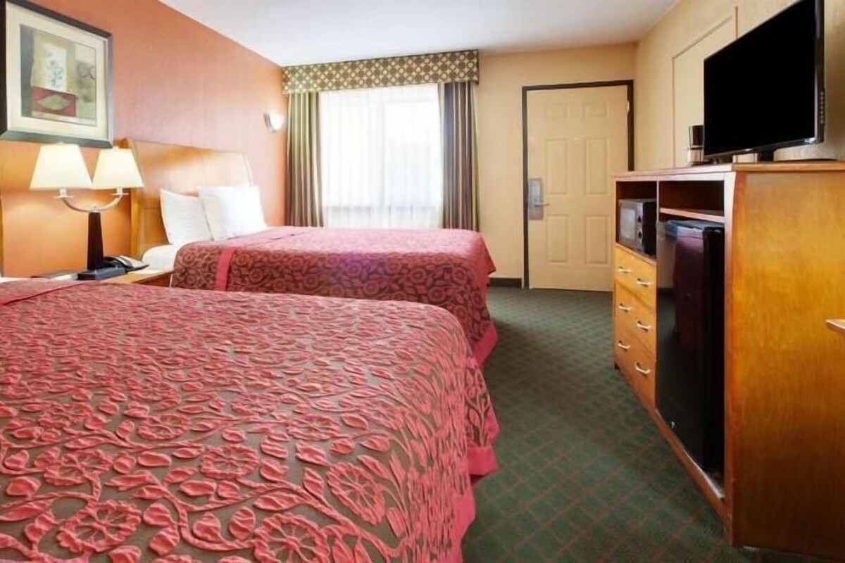 A hotel room with two beds, a television, a desk with a lamp, and a dresser.