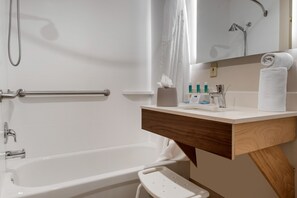 A modern bathroom with a bathtub, a shower, a vanity with a mirror, and a towel rack.
