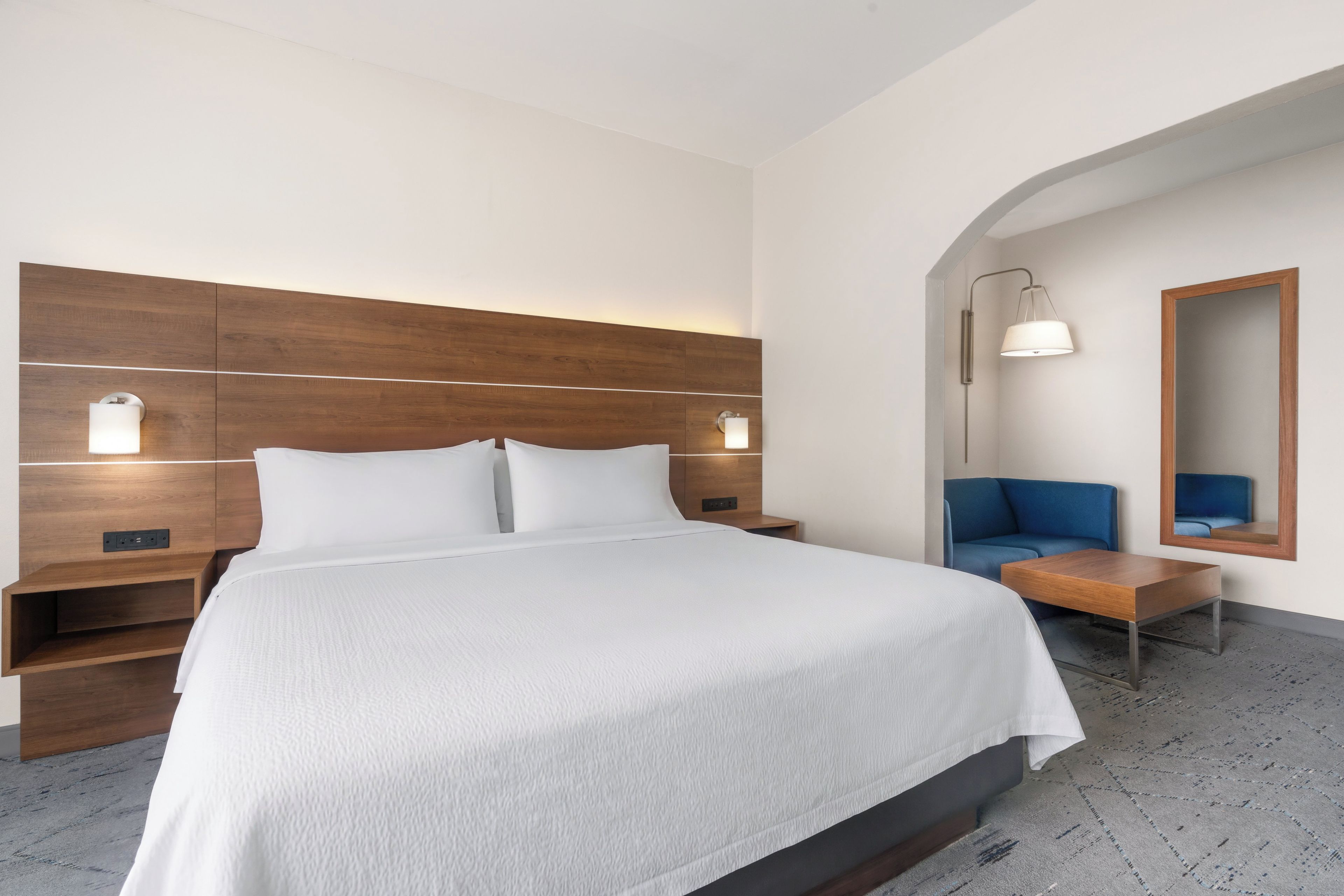 Une chambre d’hôtel avec un grand lit, des tables de chevet, un bureau, une chaise et un miroir.