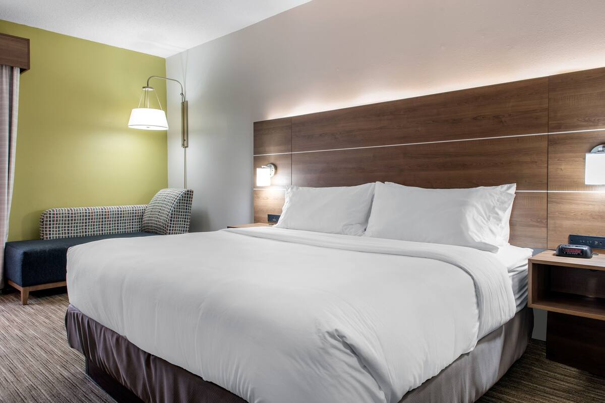 A hotel room with a large bed, a bedside table with a lamp, a small seating area with a couch, and a wooden headboard.