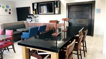 A modern dining area with a black table, wooden chairs, and a seating area with patterned cushions.