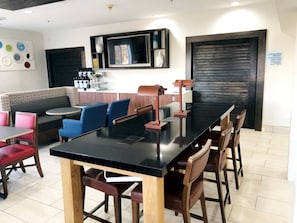 A modern dining area with a black table, wooden chairs, and a seating area with patterned cushions.