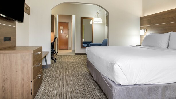 A hotel room with a large bed, a desk with drawers, a flat-screen TV, a chair, and a lamp. - Holiday Inn Express & Suites Harrison by IHG (Harrison)