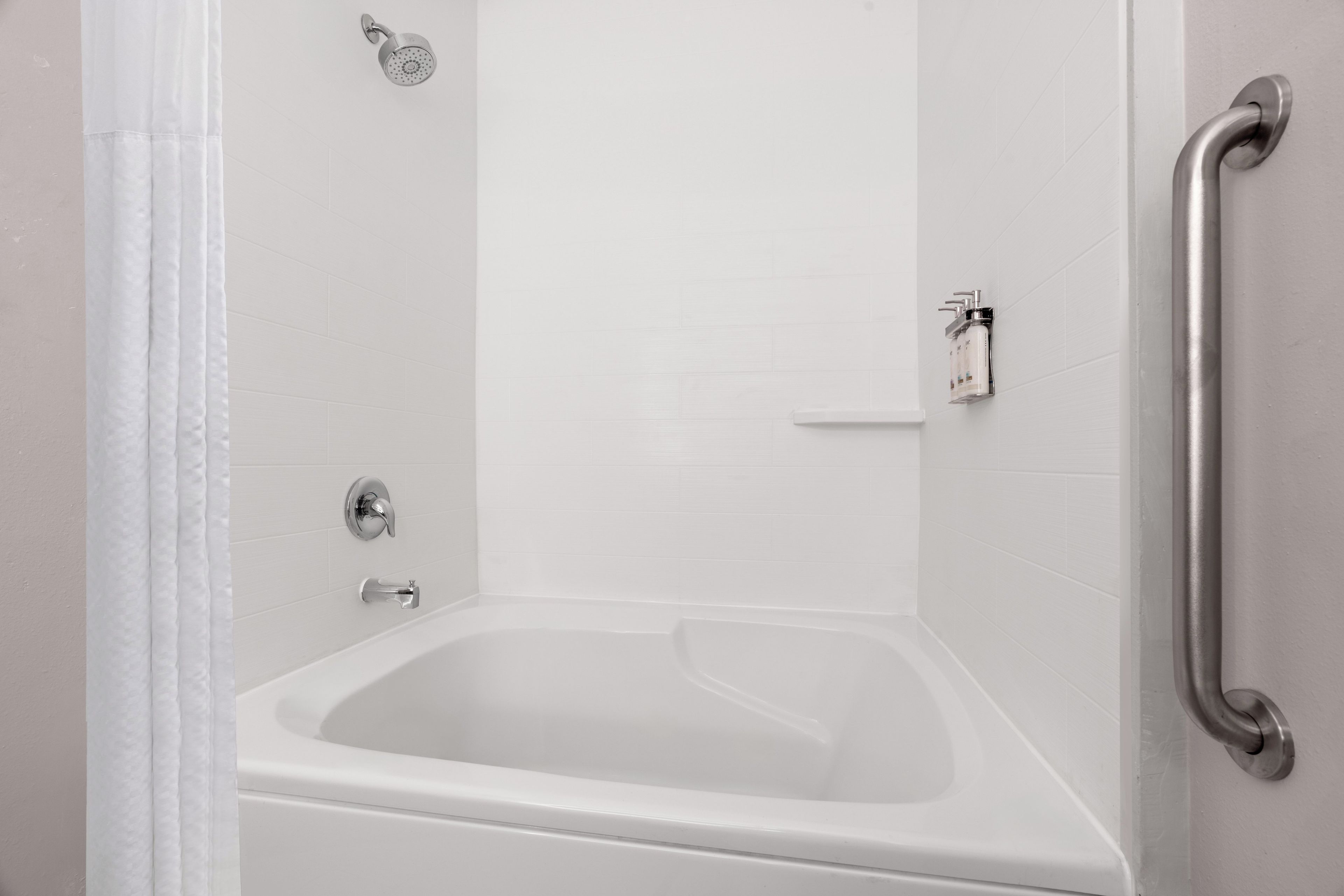 A white bathtub with a showerhead and a handrail.