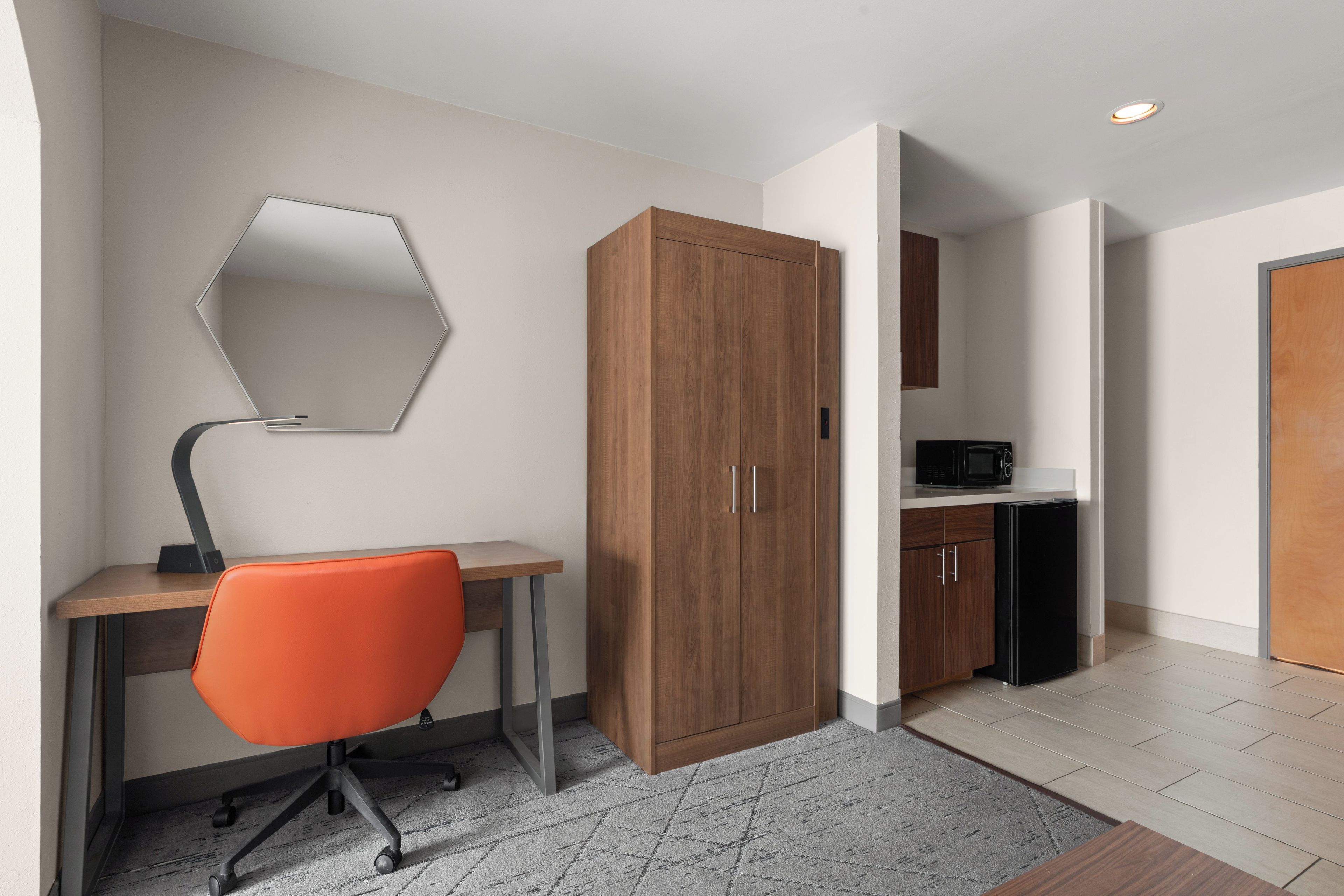 A modern office space with a desk, chair, wardrobe, and kitchenette.