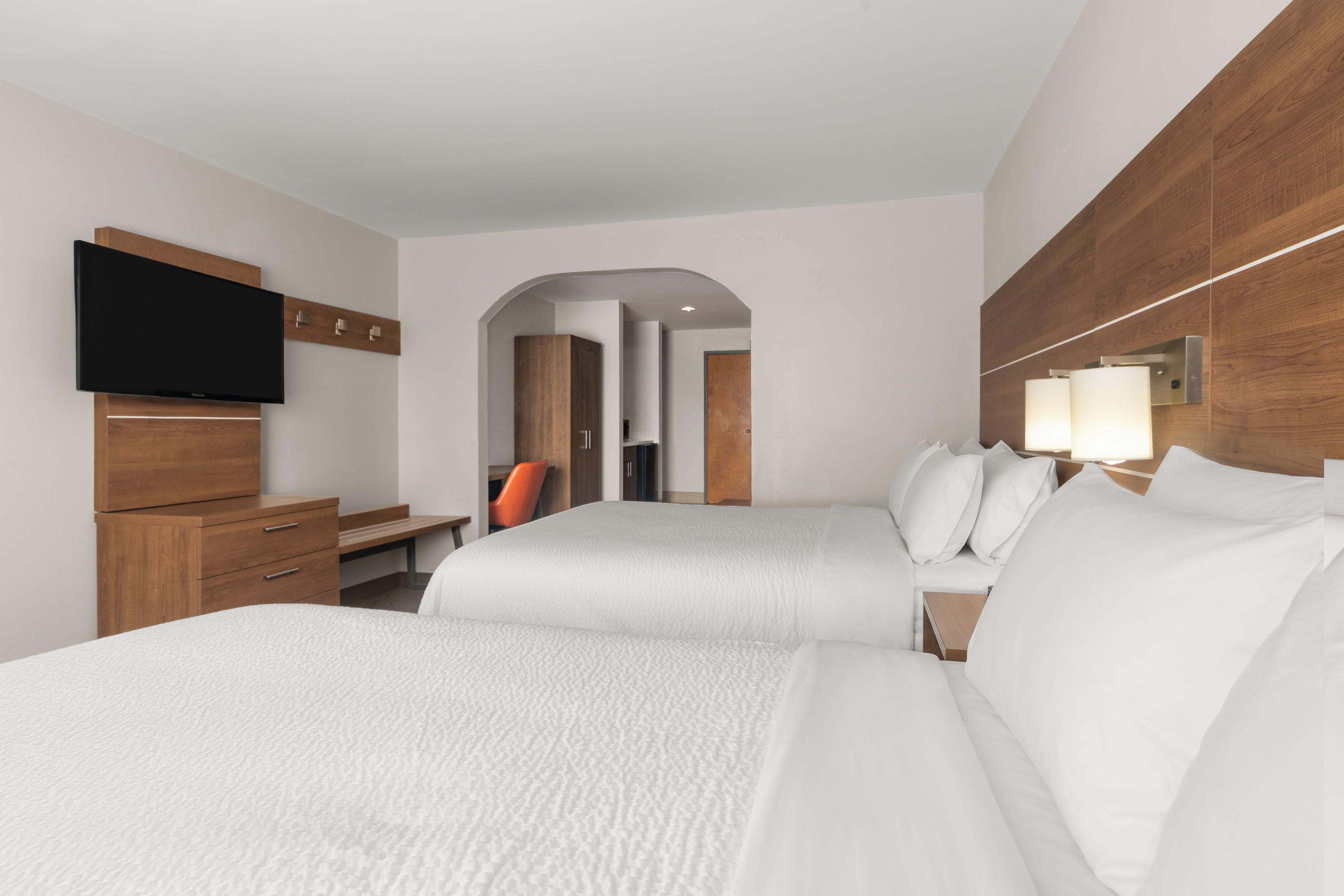 A hotel room with two beds, a desk, a television, and a mirror.