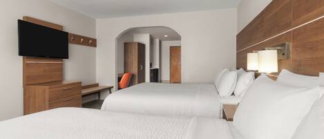 A hotel room with two beds, a desk, a television, and a mirror.