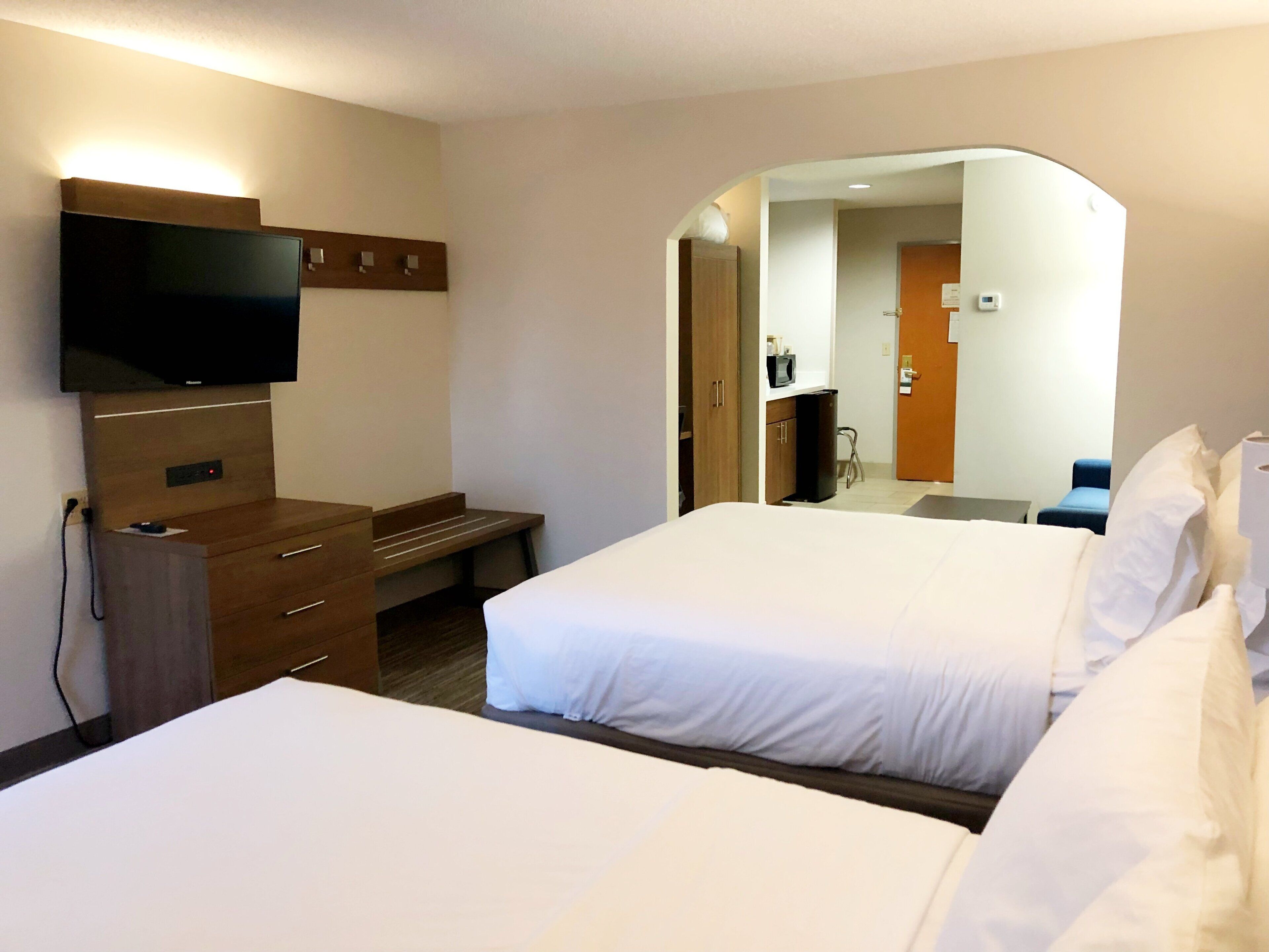 A hotel room with two beds, a desk, a flat-screen TV, and a mirror.