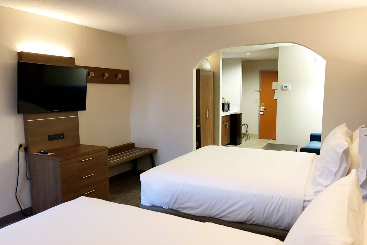 A hotel room with two beds, a TV mounted on a wooden dresser, a desk, and a mirror.