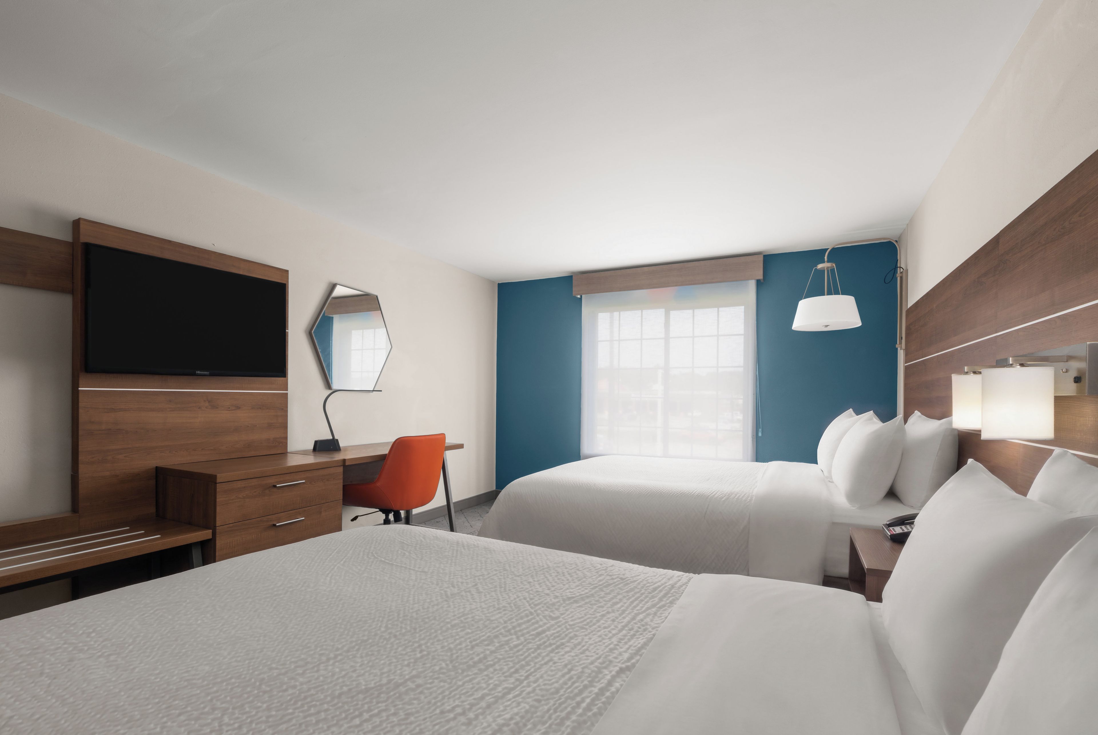 Une chambre d’hôtel avec un lit, un bureau, une chaise, une télévision et une fenêtre.