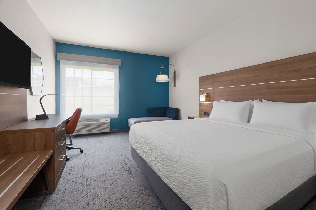 Quarto de hotel com cama, escrivaninha, cadeira, televisão e janela.
