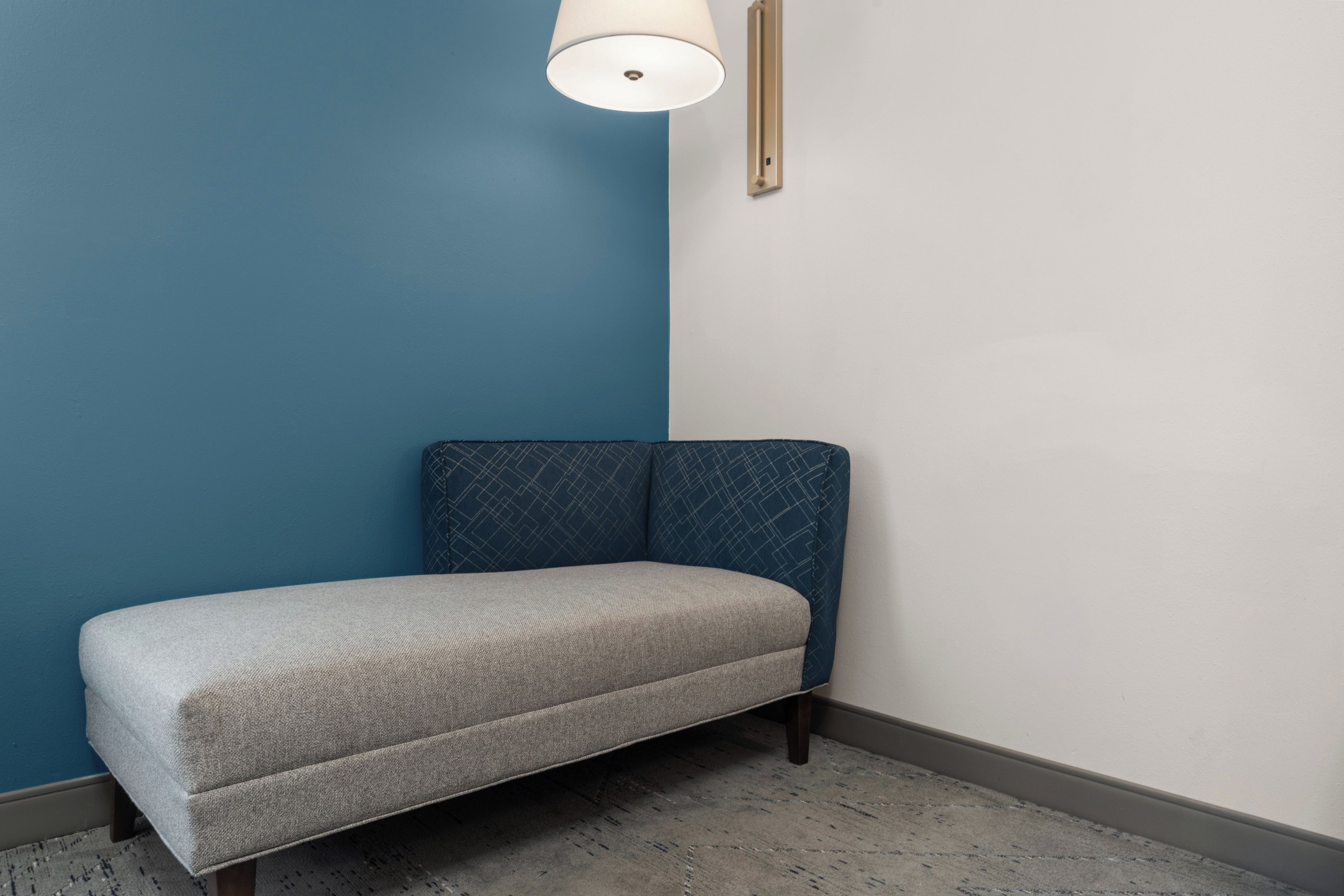 Canto de um quarto com parede azul, um banco cinzento e luminária branca no teto.