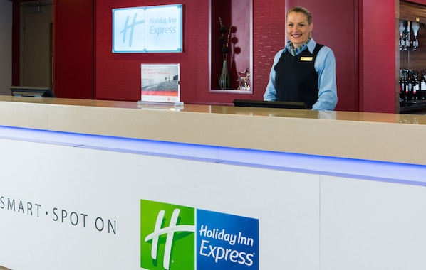 A Holiday Inn Express reception desk with a red wall, a bar area, and a sign indicating the hotel's name.