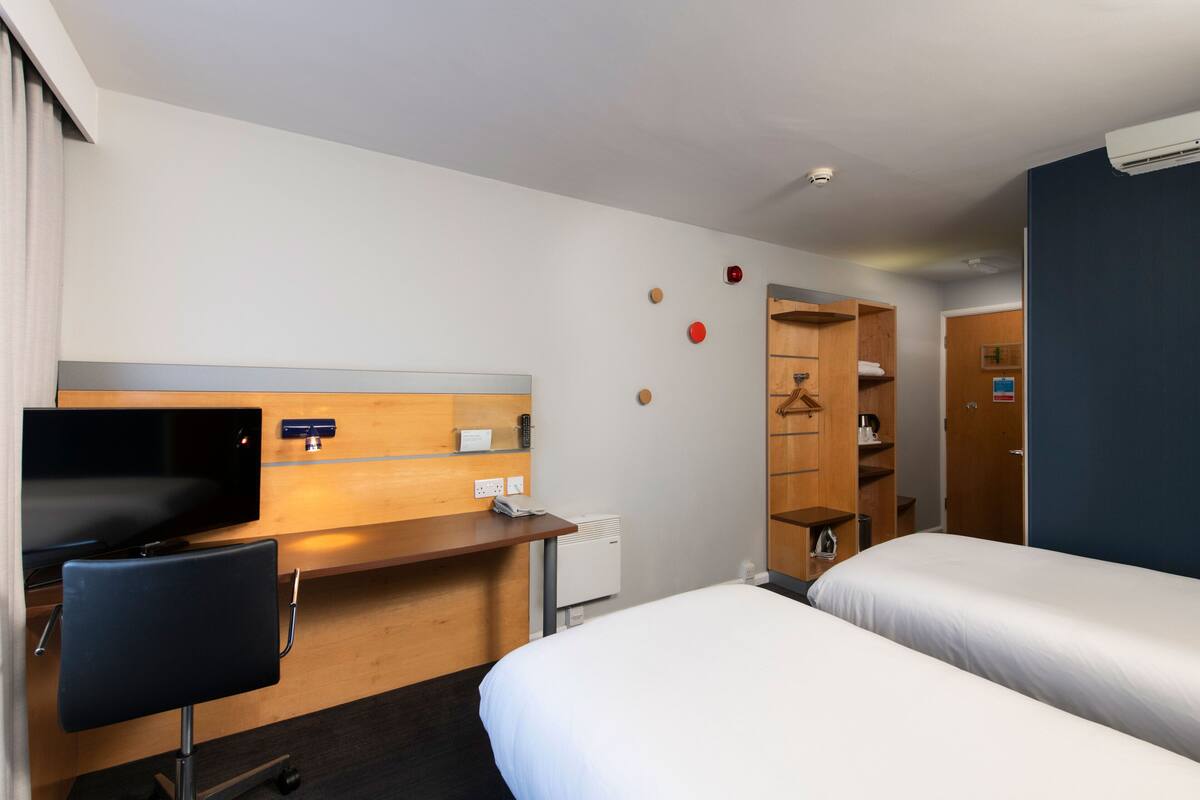 Une chambre d’hôtel comprenant un lit, un bureau avec une chaise, une télévision et une armoire.