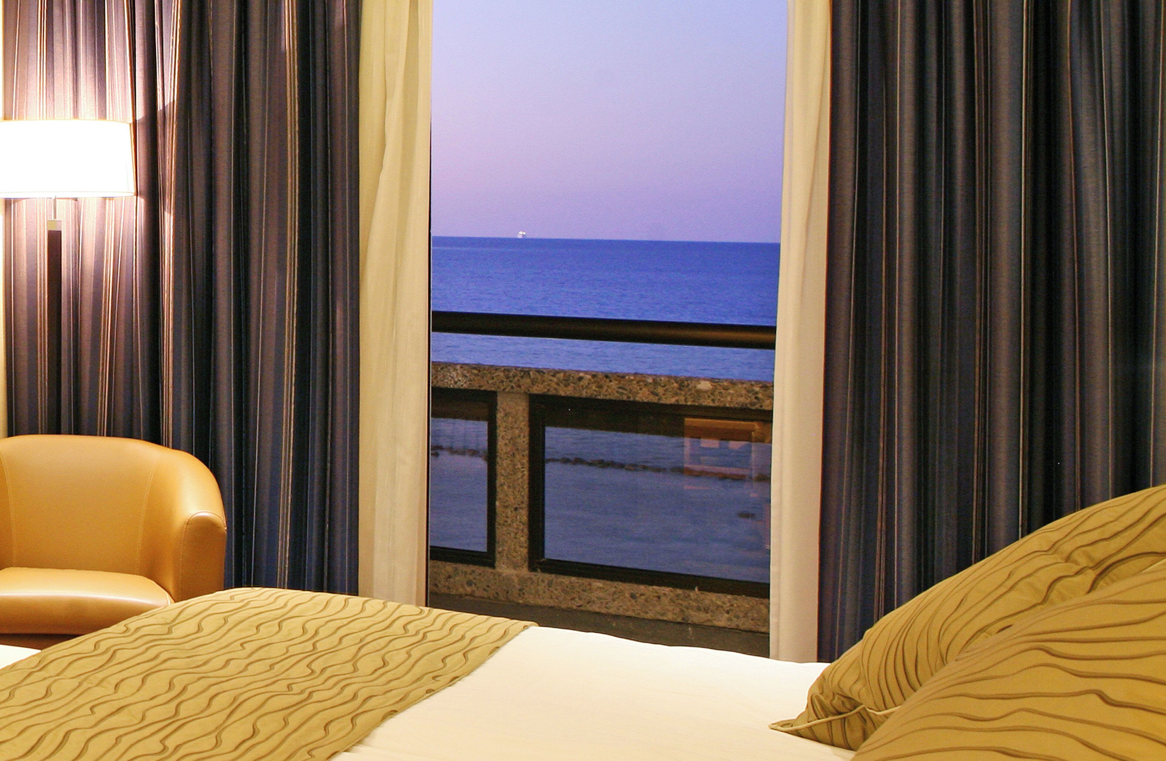 A hotel room with a bed, a chair, and a view of the sea through a window.