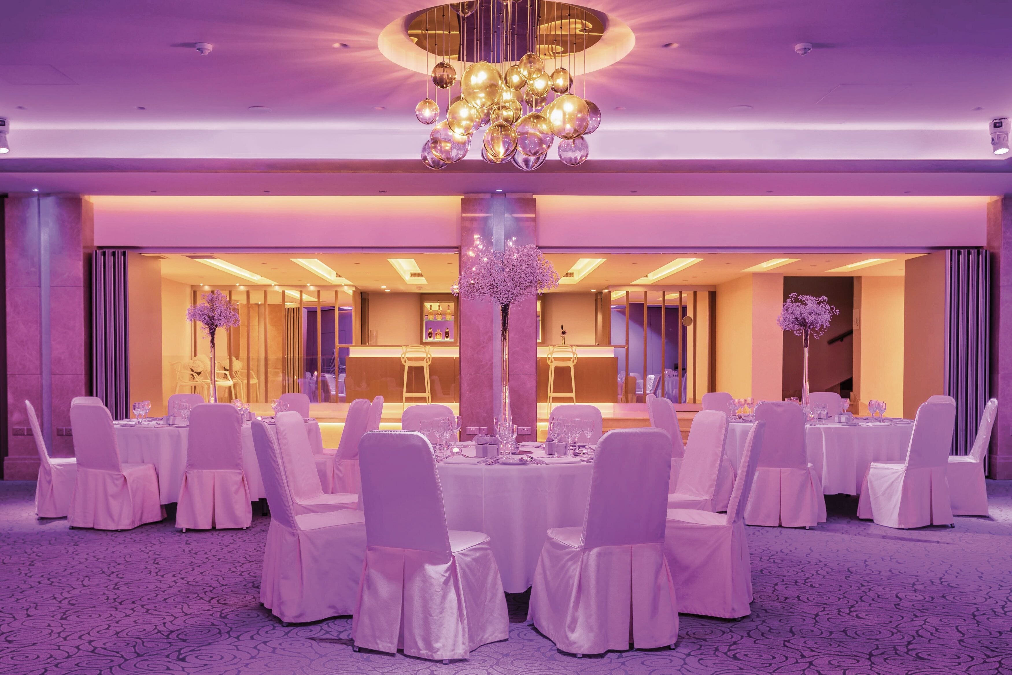 Un salón de banquetes con mesas redondas, sillas blancas y un arreglo floral central.