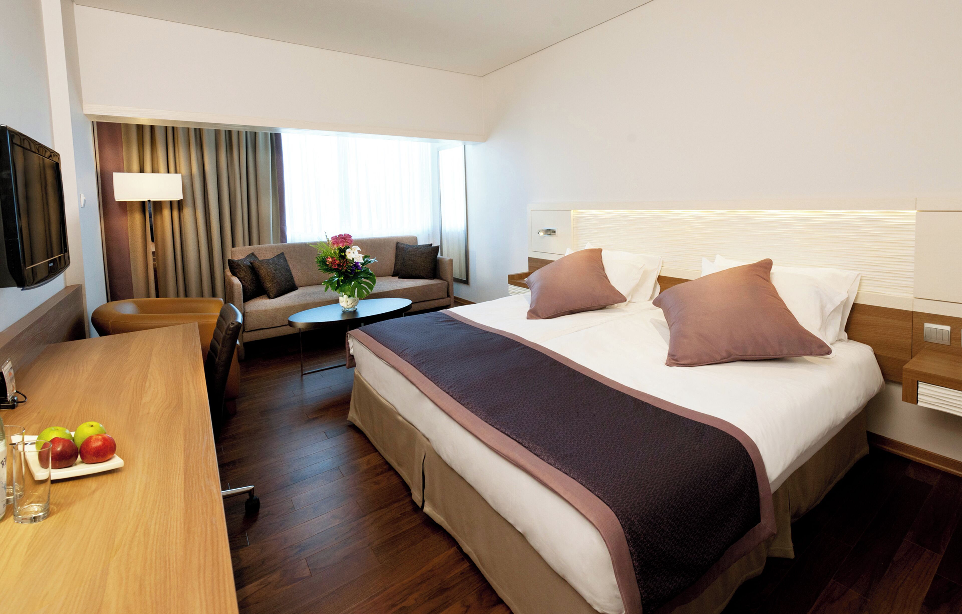 Habitación de hotel con cama, sofá, una mesa con fruta y televisor.