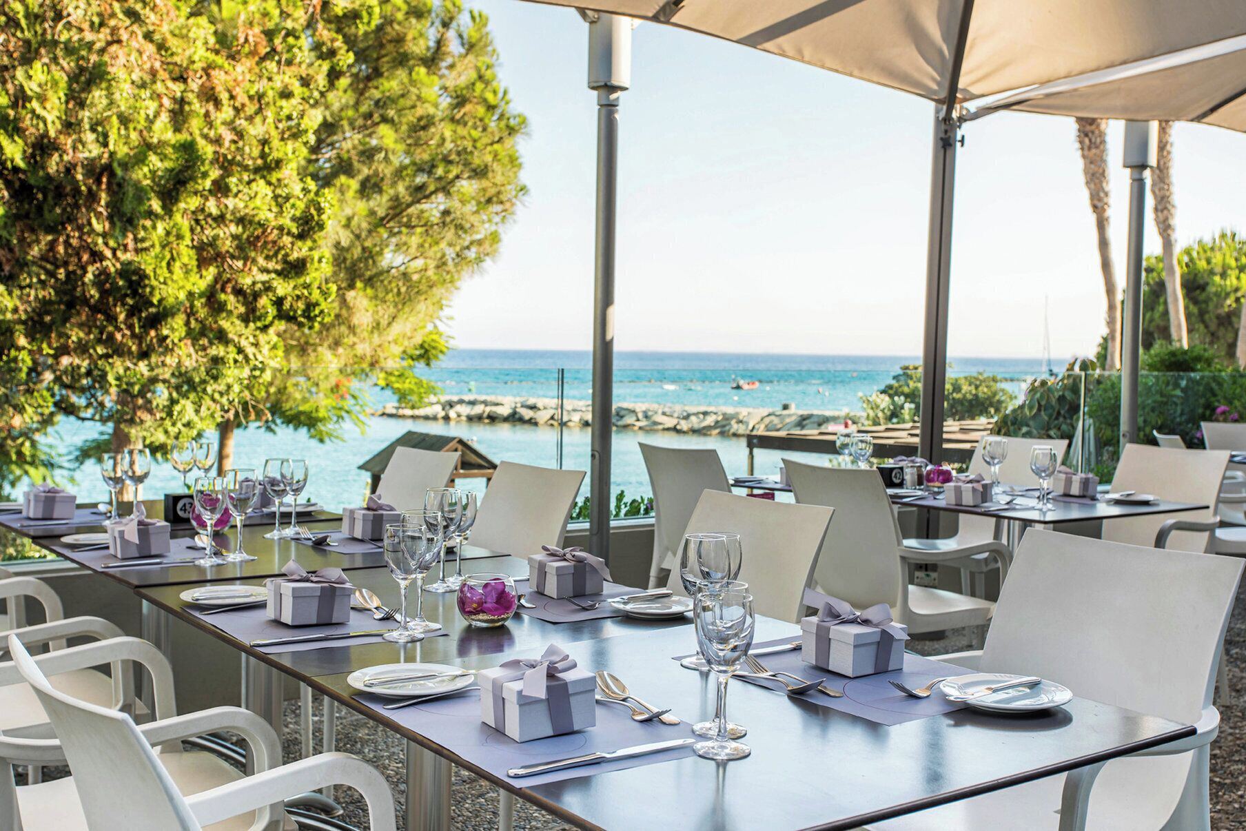 Un área de comedor al aire libre con mesas dispuestas para una comida, con vista a un cuerpo de agua.