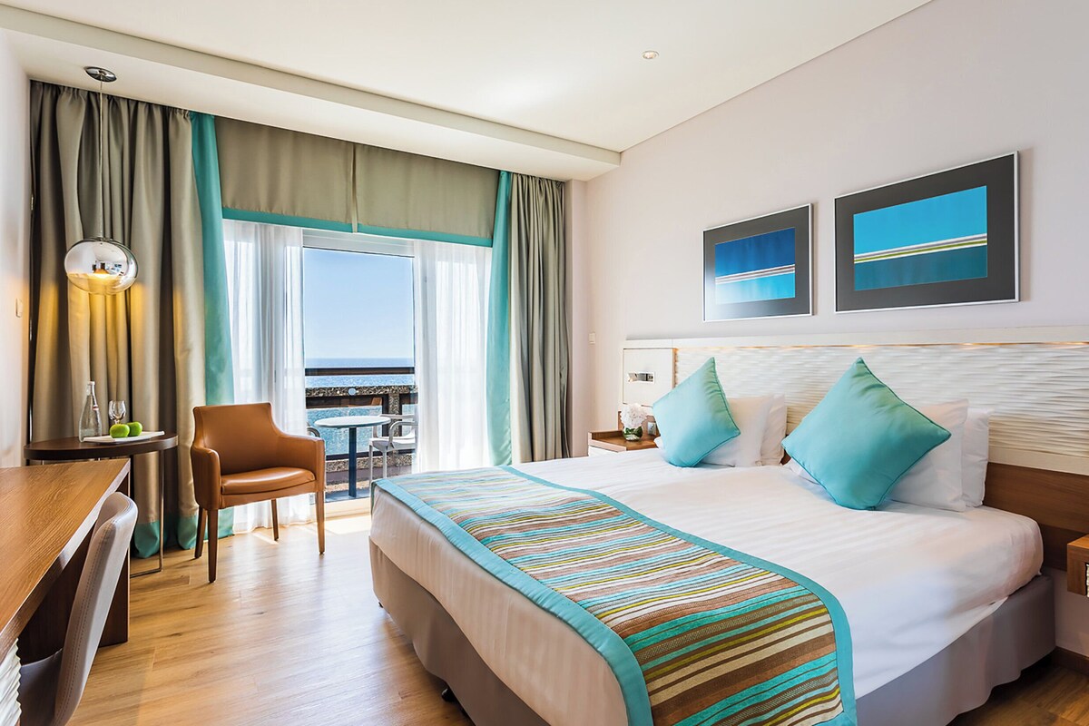 Une chambre d’hôtel avec un grand lit, un bureau, une chaise et une vue sur l’océan.