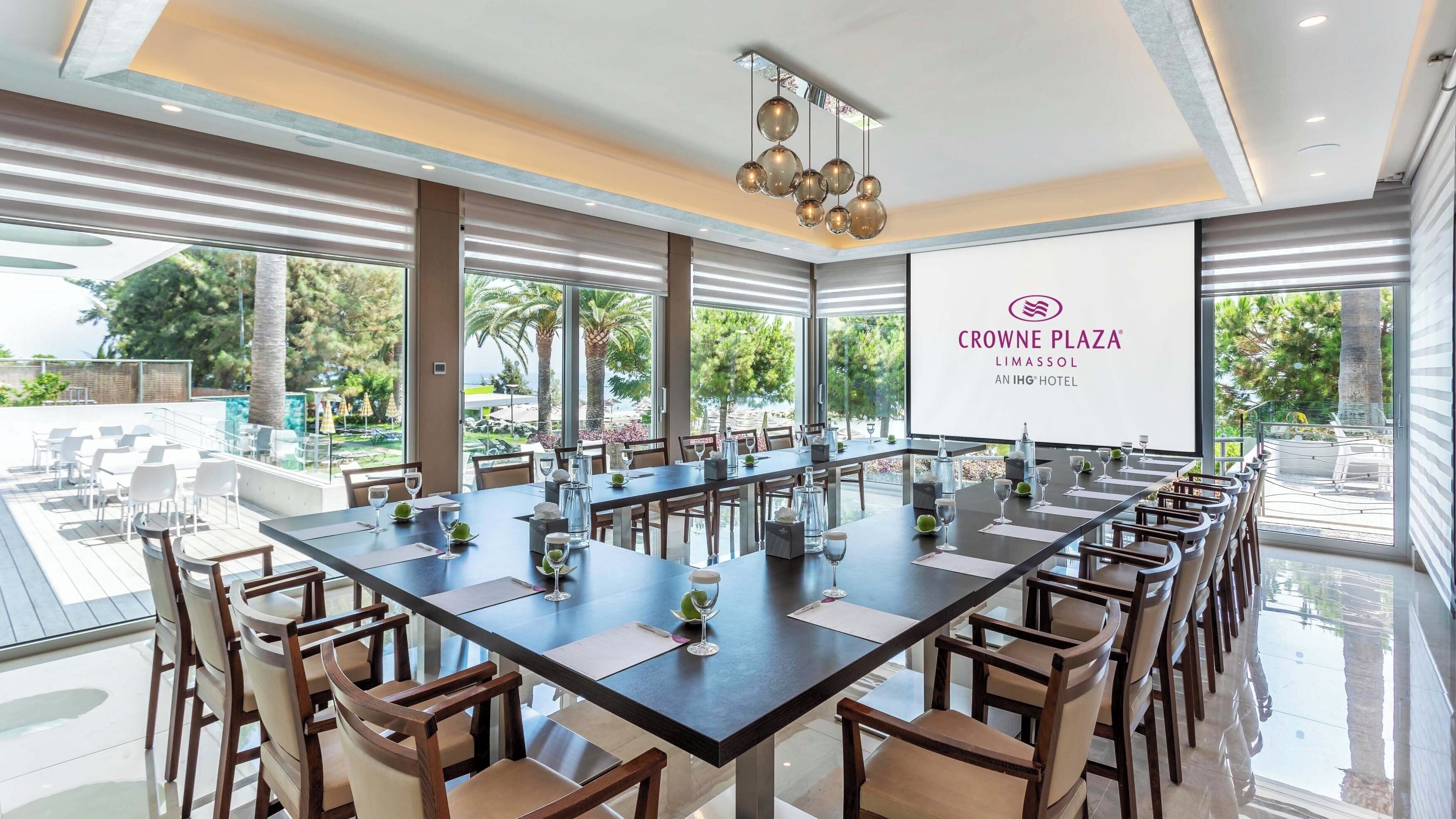 Un salón de conferencias con una larga mesa, sillas y una pantalla grande que muestra el nombre del hotel.