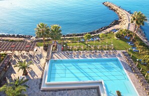 Una piscina con tumbonas y palmeras, con vistas a una costa rocosa.