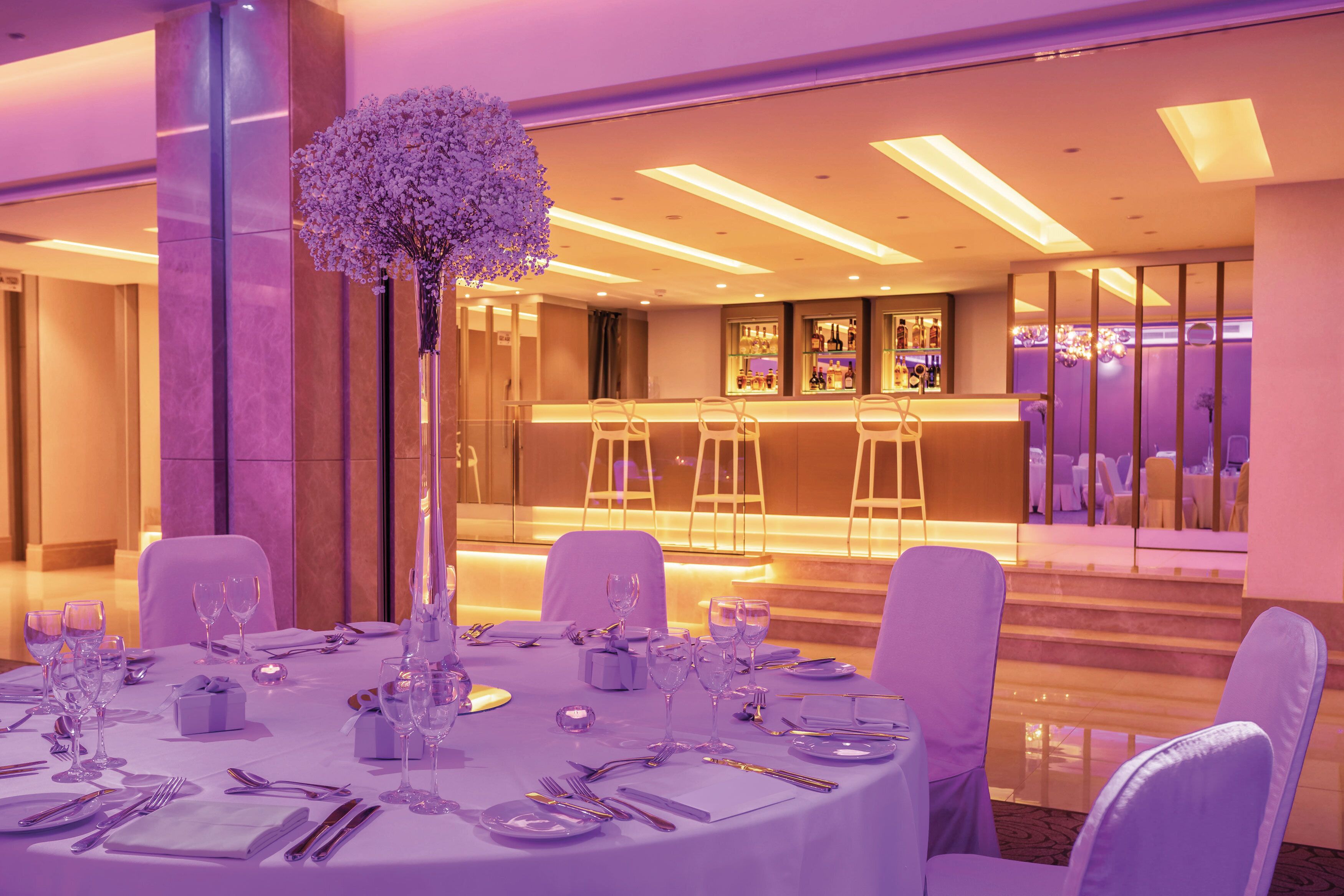 A well-lit, elegantly set dining area with a central floral arrangement, multiple tables, and chairs.