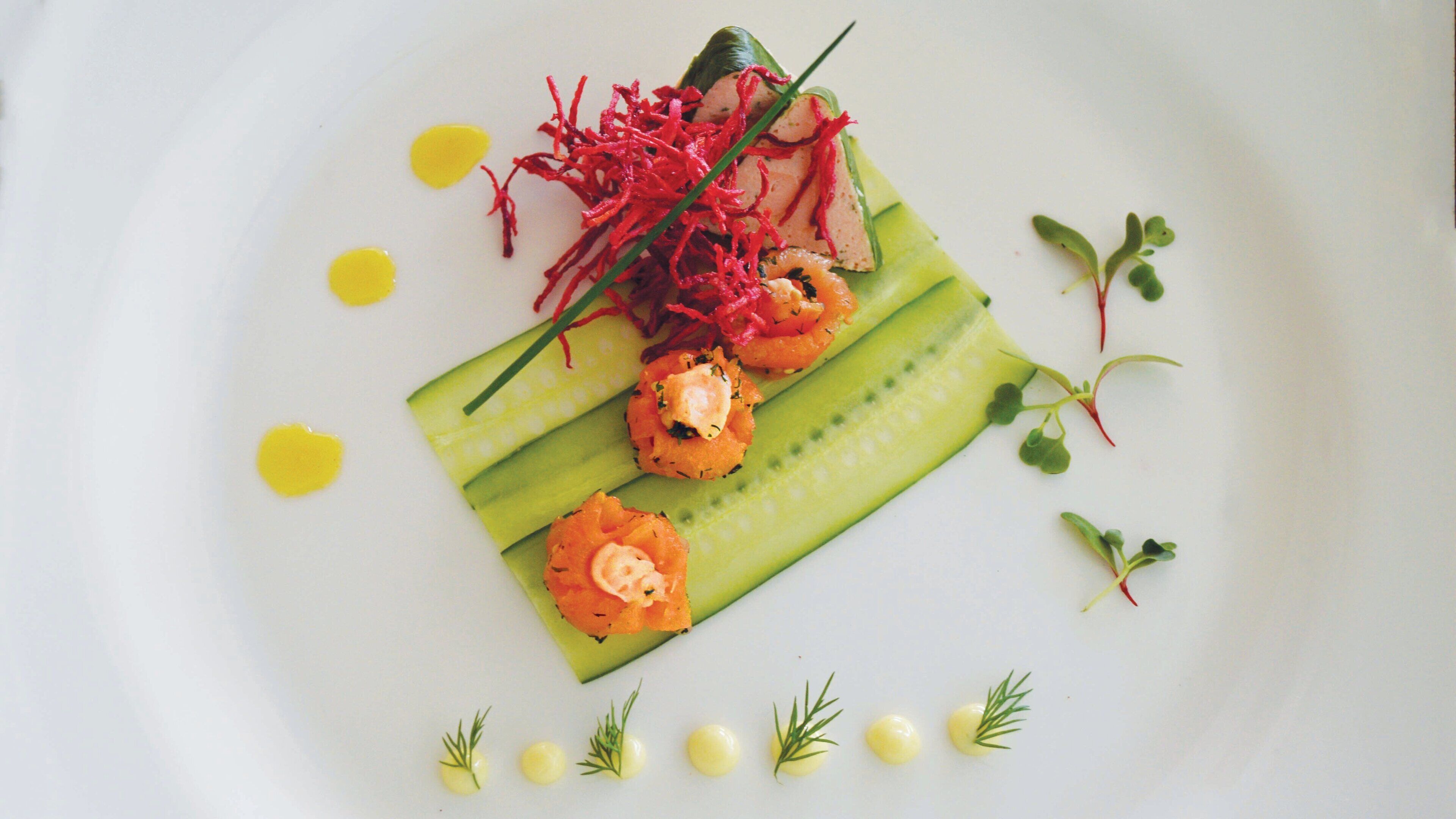 A white plate with a dish of food consisting of cucumber slices, shrimp, and garnishes.