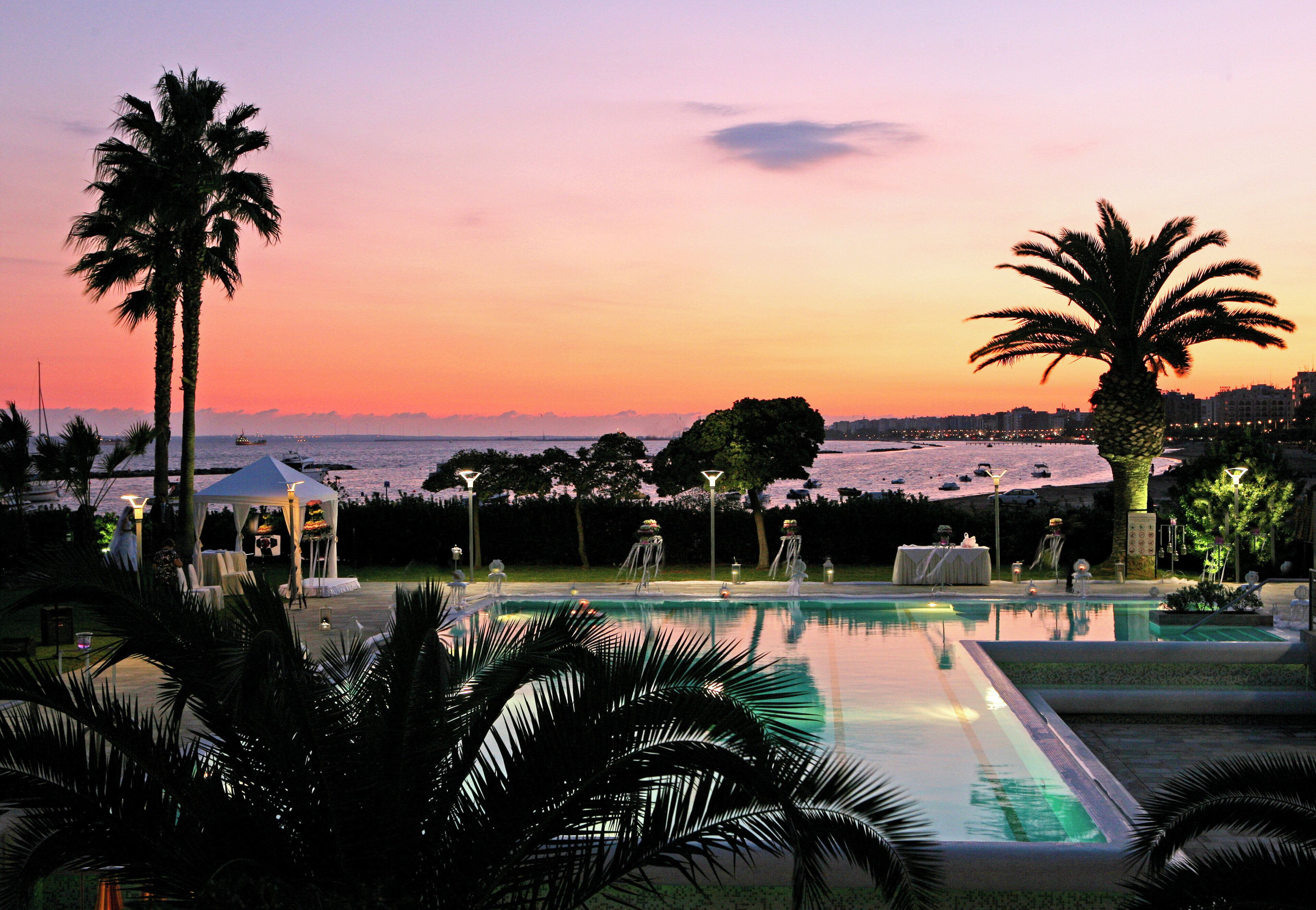 A pool area with a sunset view, palm trees, and a gazebo.