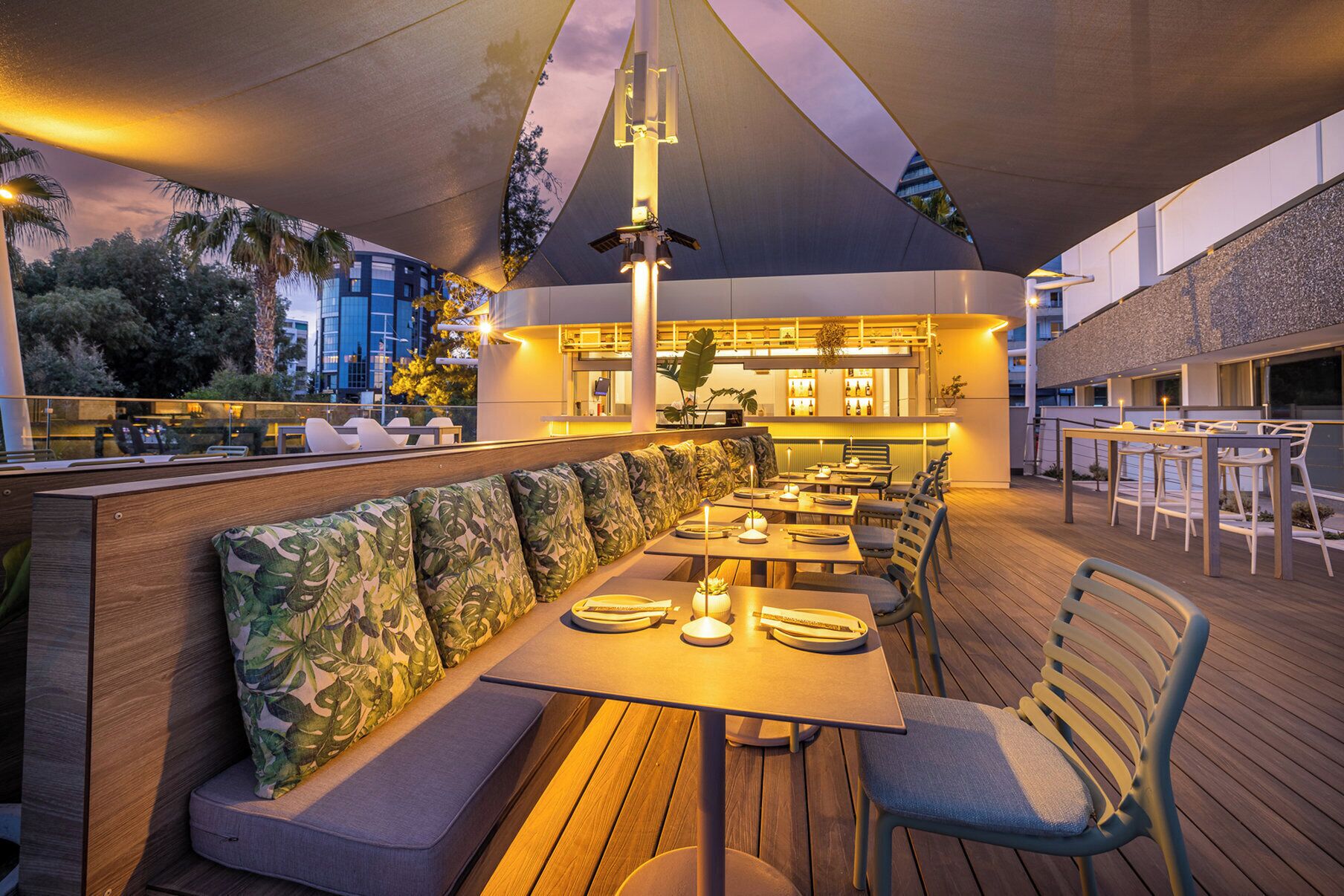 Un espace extérieur aménagé pour les repas, avec des tables et des bancs en bois, un coin bar doté d’un comptoir, et un grand parasol offrant de l’ombre.