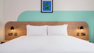 Un letto rifatto con cura, con una testiera in legno, due lampade da lettura fissate al muro e un quadro incorniciato sopra la testiera.