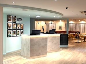 A reception desk with framed artwork, a seating area with tables and chairs, and a visible security camera. - Garner Hotel Lincoln by IHG (Lincoln)