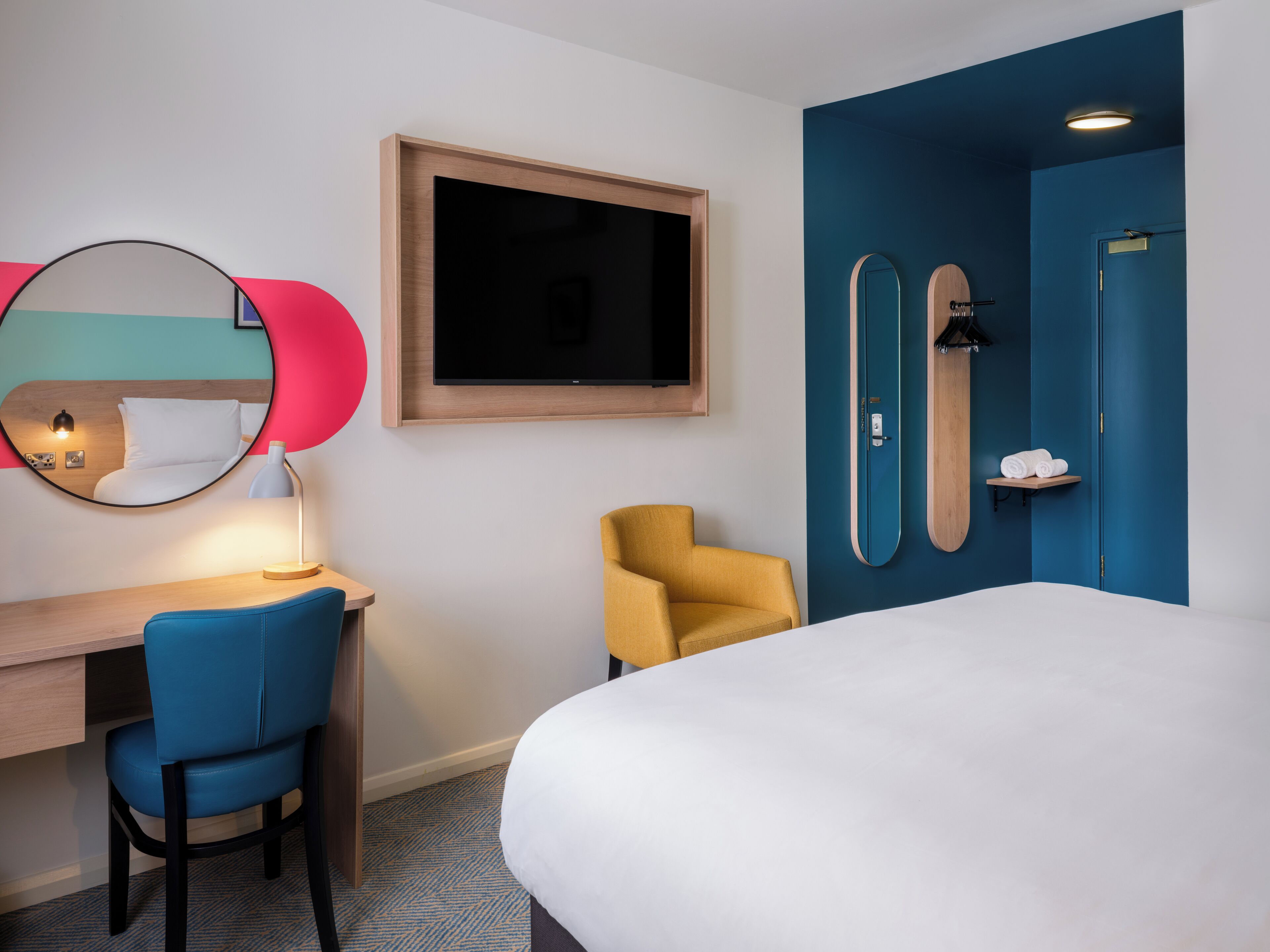 Une chambre d’hôtel comprenant un lit, un bureau avec une chaise, une télévision, un miroir, une douche et un porte-serviettes.