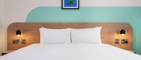 Una cama bien hecha con sábanas blancas, cabecera de madera y dos lámparas de lectura fijadas a la pared.