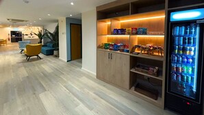 A hotel lobby with a vending machine, seating area, and a wooden cabinet with snacks.