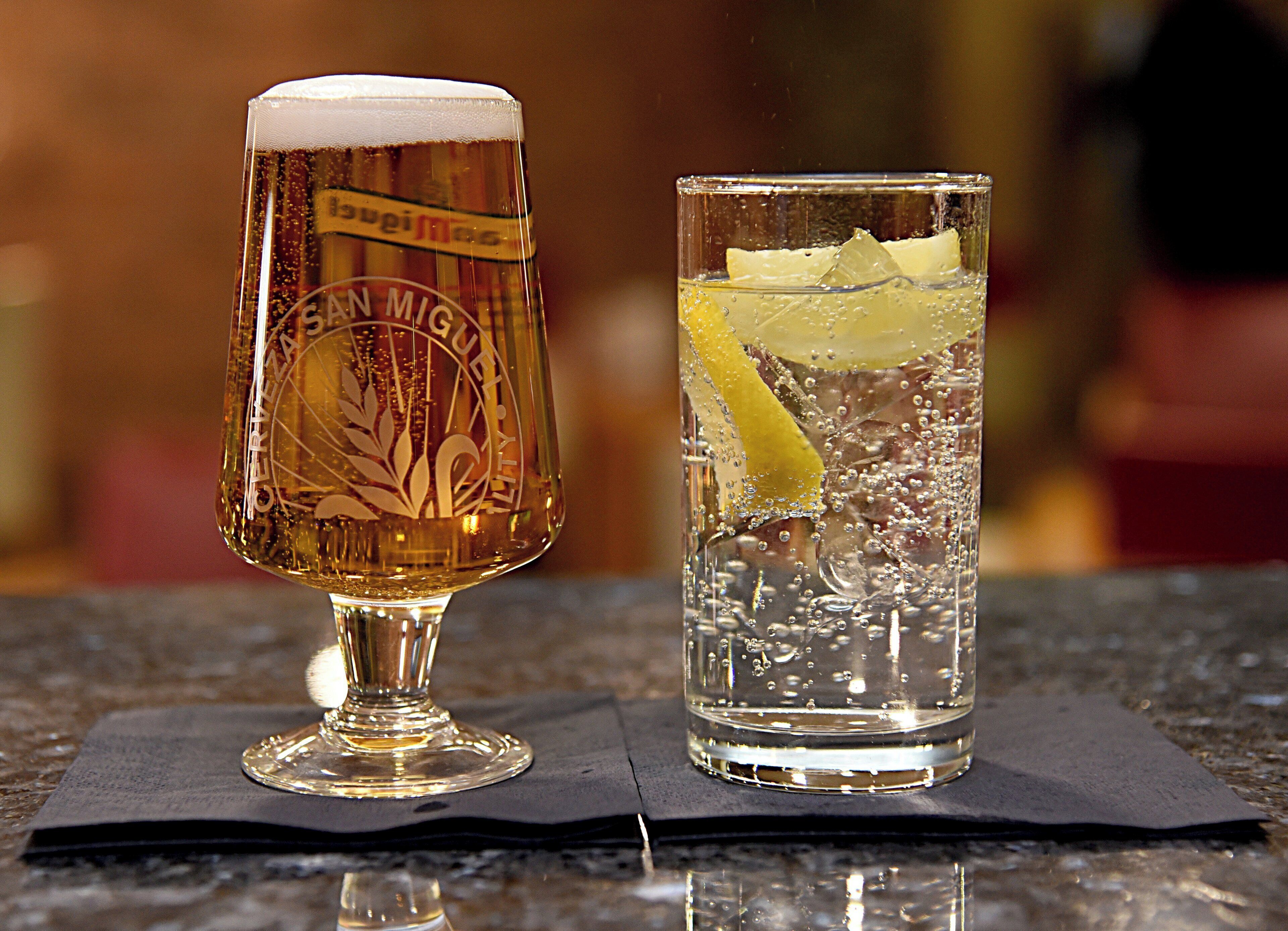 To glas med drikke, hvoraf det ene har et skumlag og det andet et citronskive, på en mørk overflade.