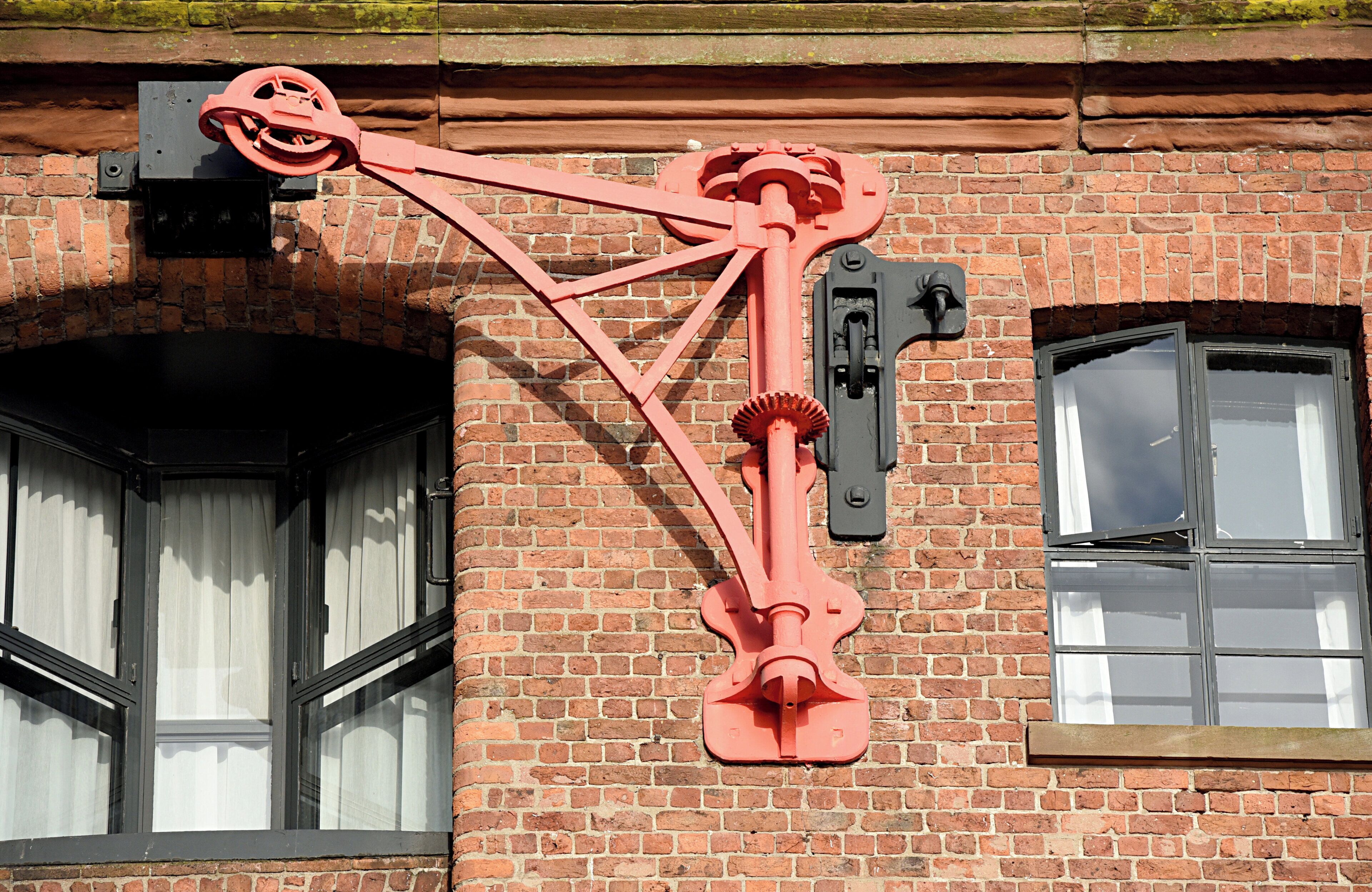 Un dispositivo mecánico rojo adherido a un edificio de ladrillo con una ventana.