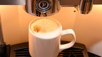 A white cup with a frothy top, placed on a black surface with a logo.