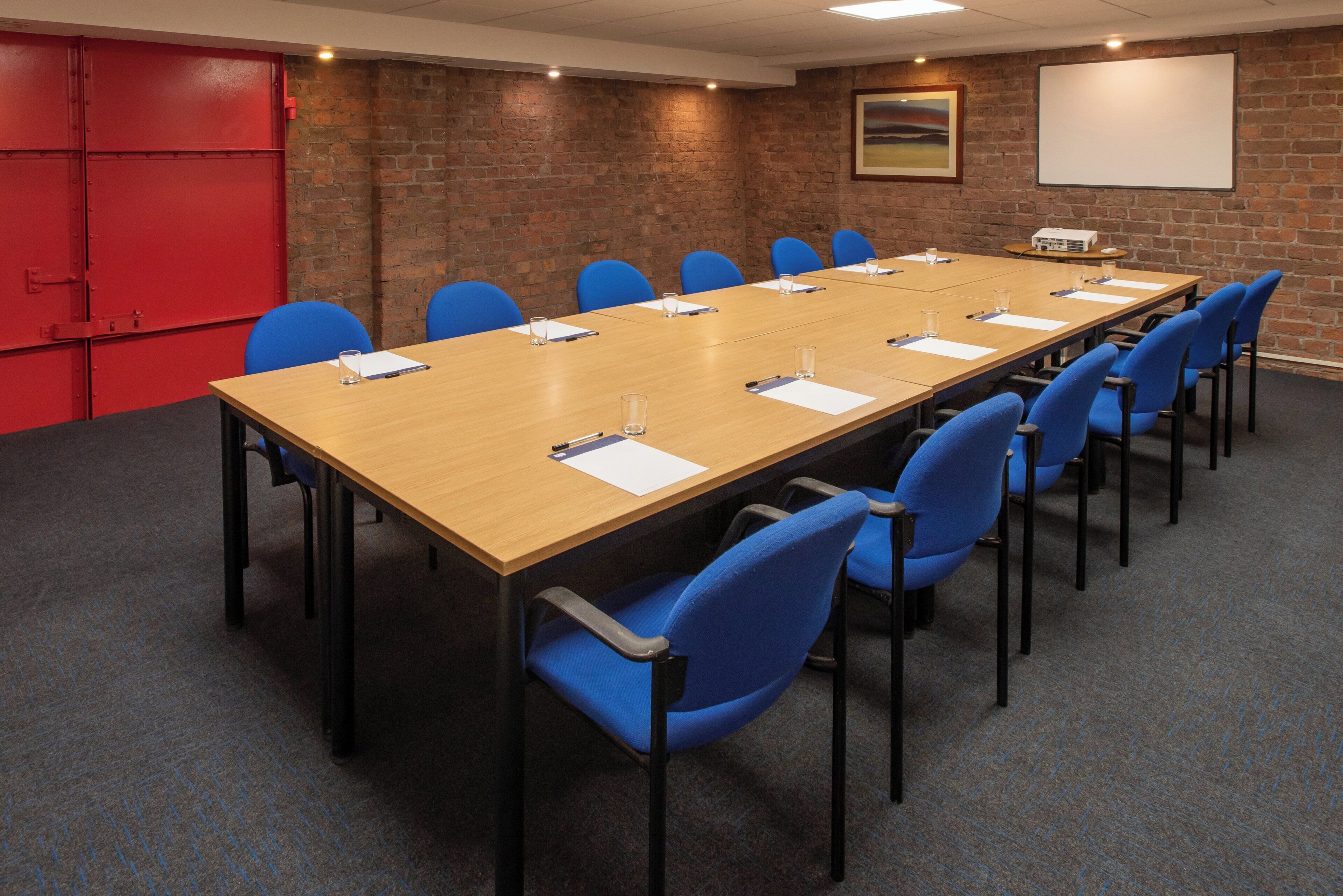 A conference room with a long table, blue chairs, a projector, and a whiteboard.