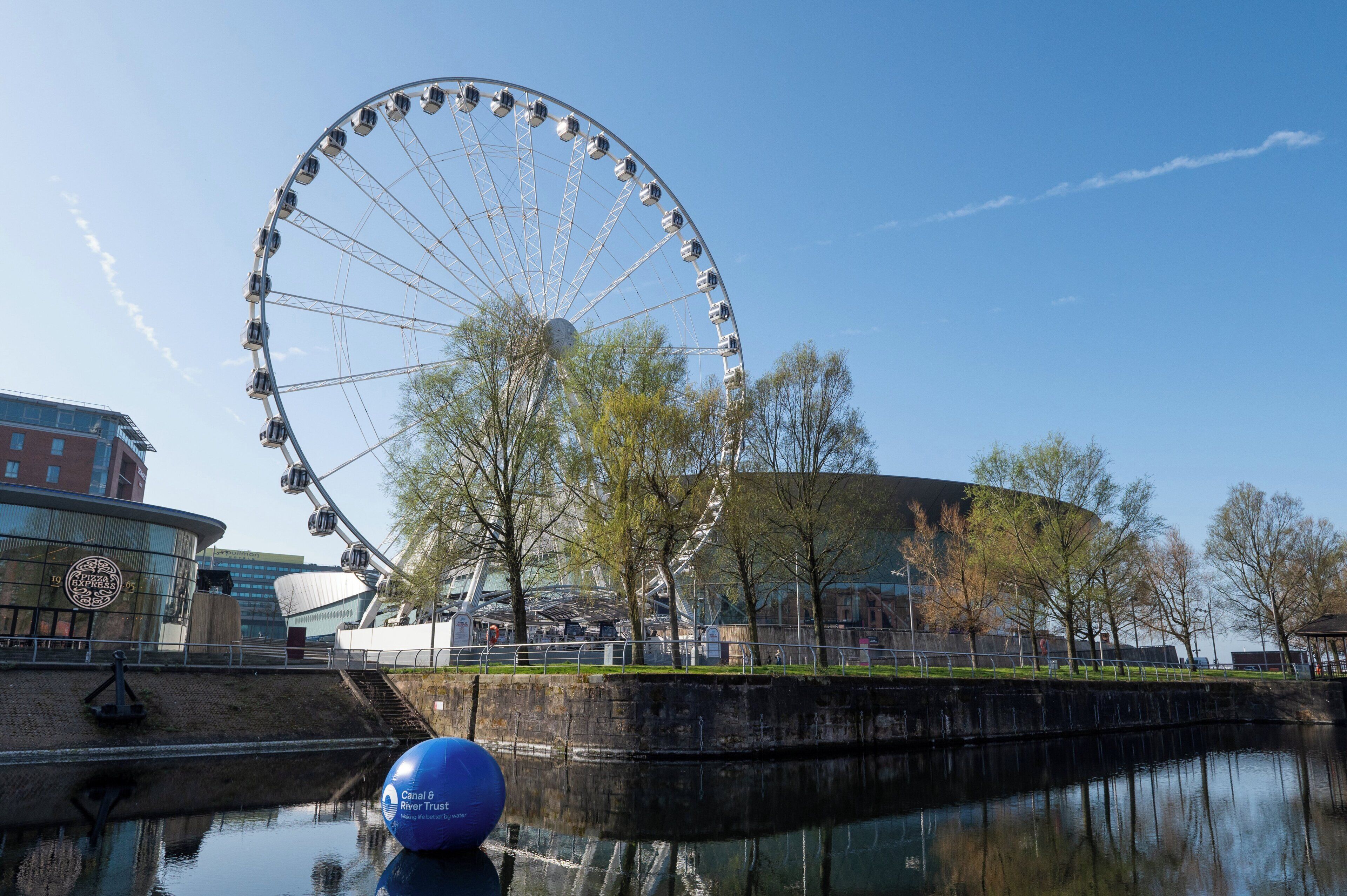 A Ferris wheel, a body of water, and a modern building with a glass facade.
