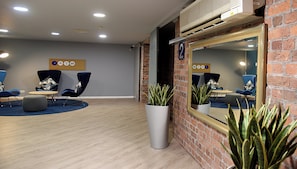A modern waiting area with a brick wall, a large mirror, and a seating area with chairs and a round table.
